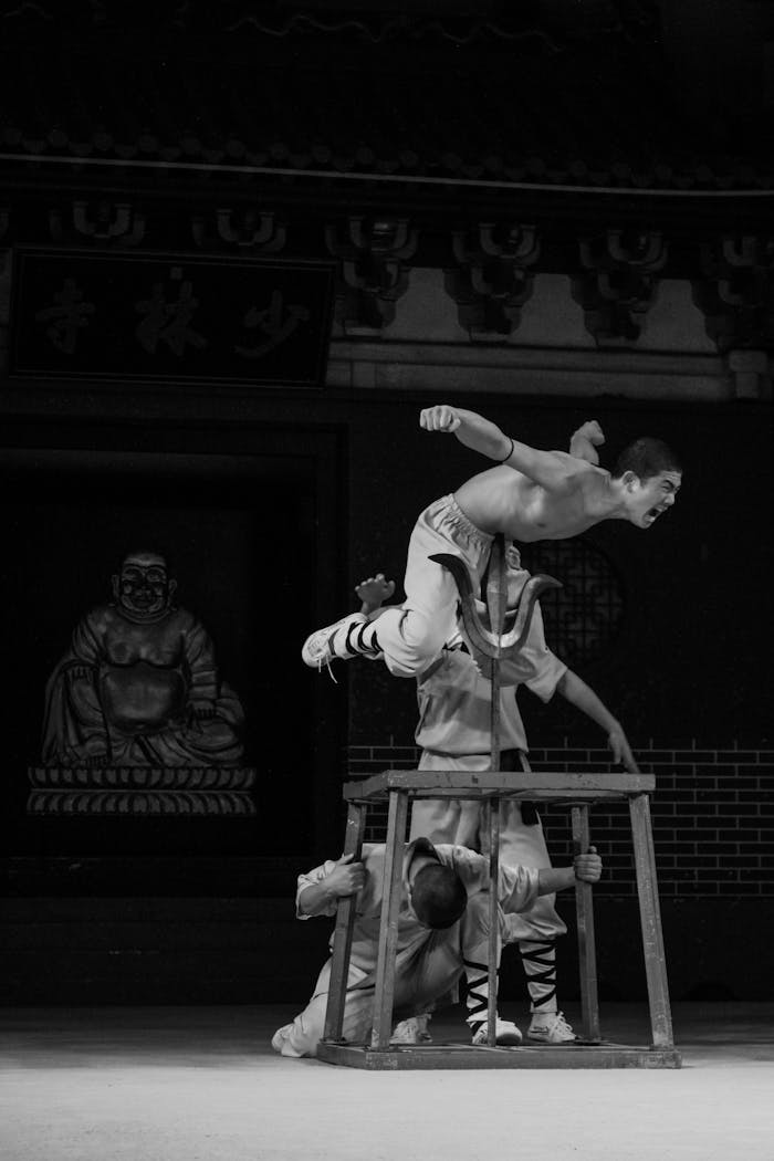 Black and white photo of a martial arts display with two men showcasing acrobatic skills indoors.